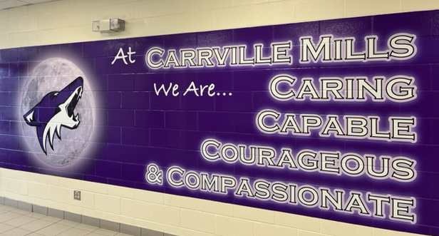 Section of school wall painted purple with image of howling wolf and words "at Carville Mills, we are caring, capable, courageous and compassionate."
